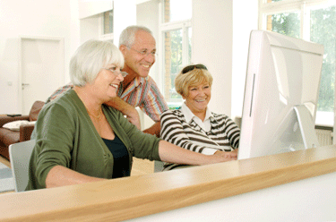 three seniors happily looking at computer monitor