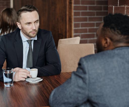 Two people sit together drinking coffee. One person's expression is difficult to read. Is it interest? Disdain? Boredom?