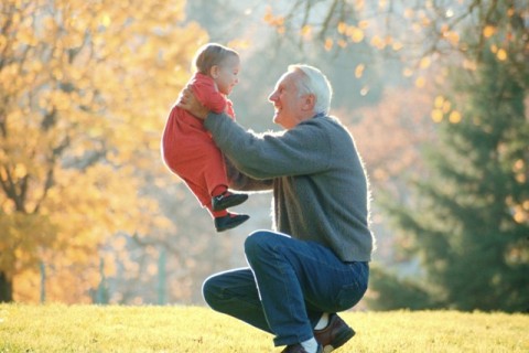 grandfather lifting grandchild into air with autumn tree background