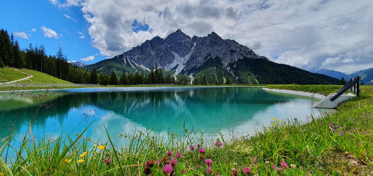 A glacier mountain lies in the distance with turquoise glacial waters in the foreground. A rich forest surrounds the mountain