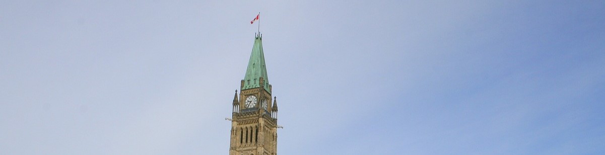 The Canadian Parliament Building's Clock Tower with a Canadian flag on the top of the peaked roof