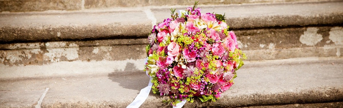 A bouquet of flowers on a concrete staircase. Flowers are pink and yellow, and there is a white ribbon tied to the bouquet