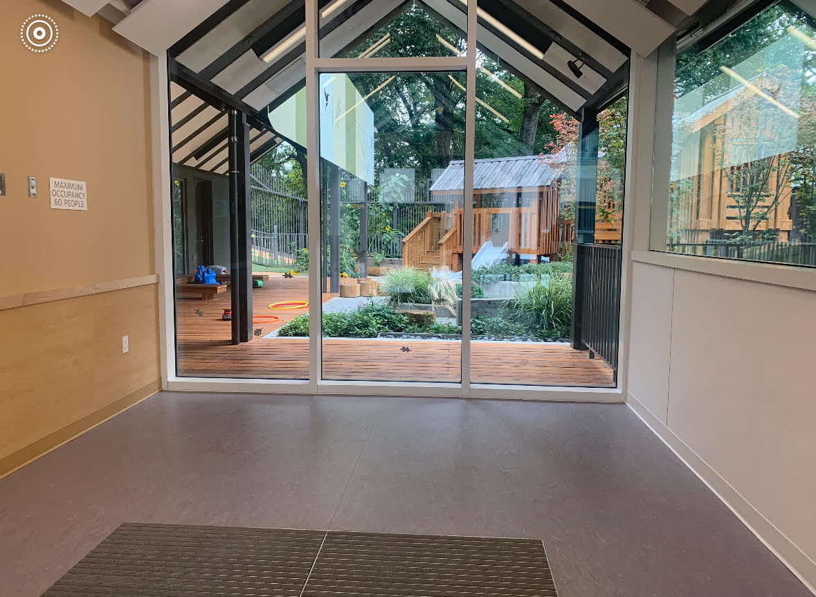 An empty room with large windows and a door leading to a lush backyard patio with a wooden playhouse in the background