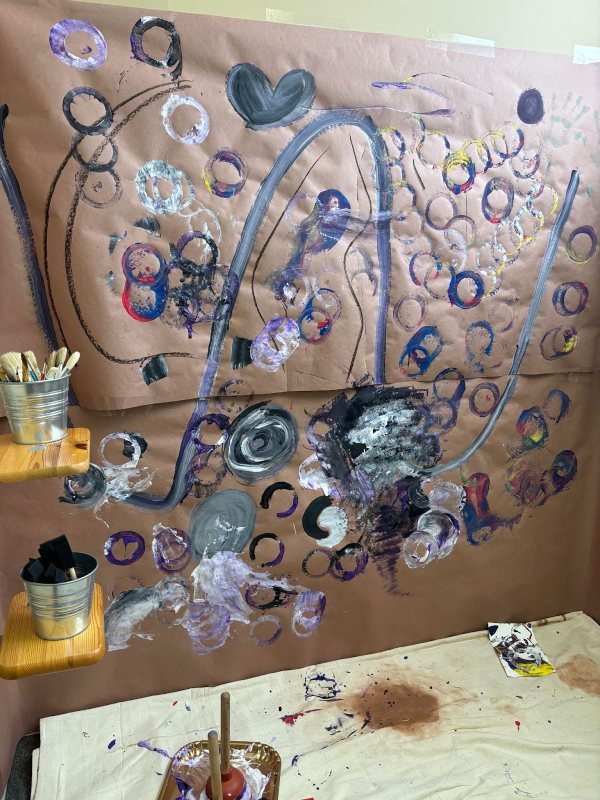 Kraft paper is covering a wall with children's art on every inch, including paint lid circles, painted hearts, swooping lines