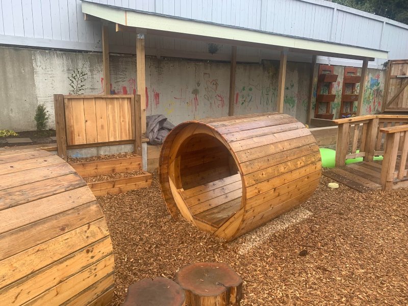 An outdoor ECE centre play space with wooden structures to climb through and in