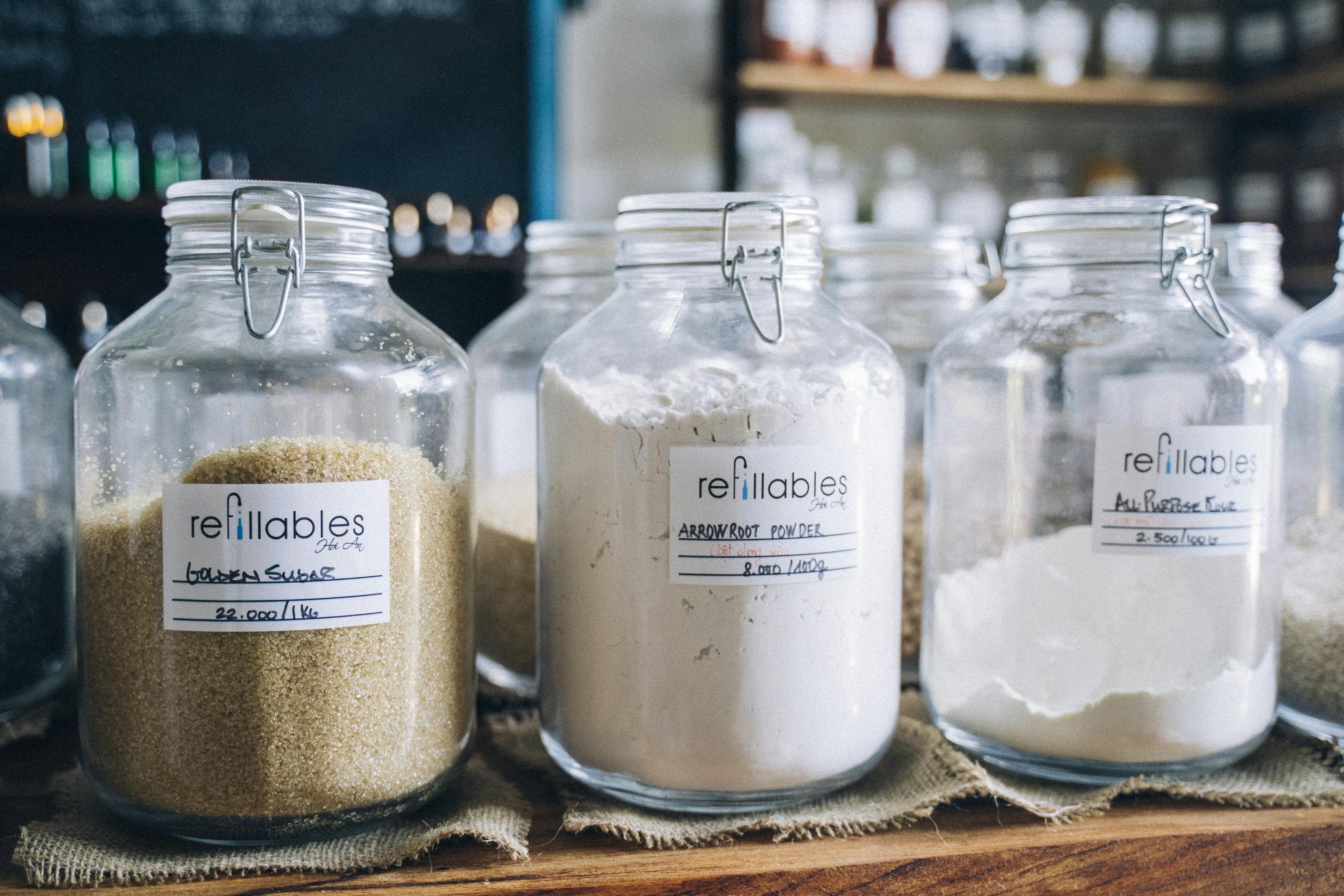 three clear glass jars sit on a counter filled with flower, sugar and baking soda and each is labelled with contents listed