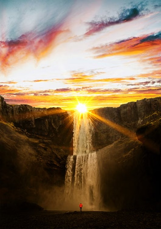 A sunset casts vibrant colours over a powerful waterfall surrounded by cliffs.